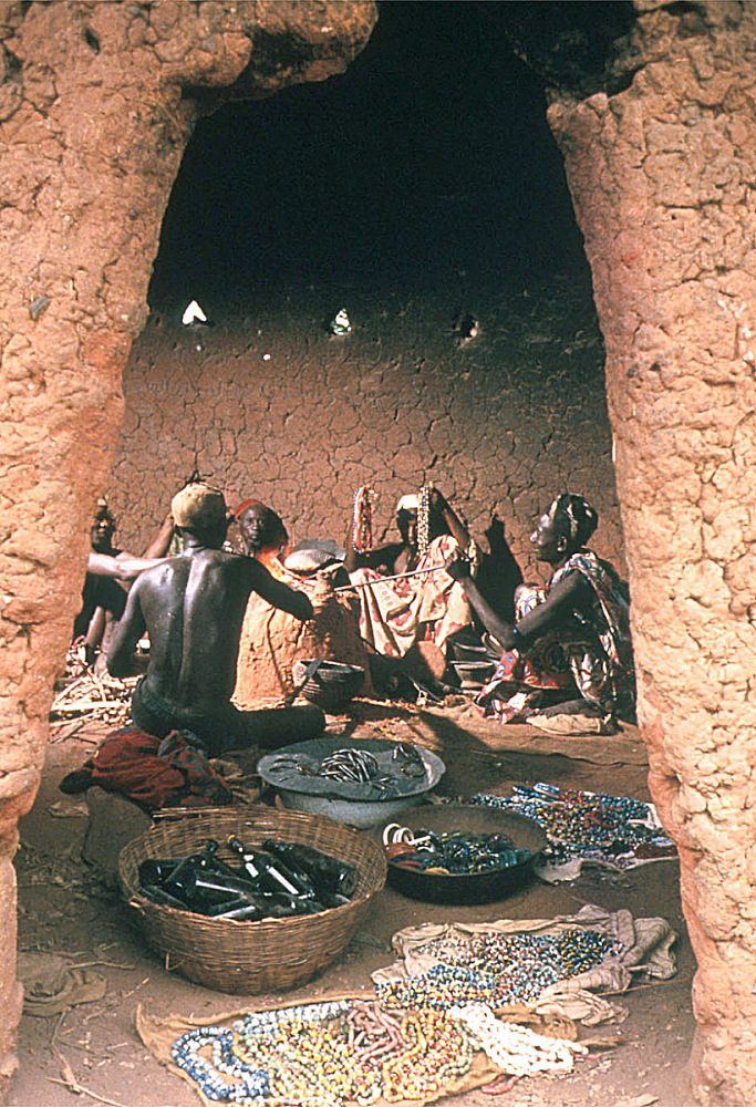 People seated at a compound doorway with strands of beads laid out in trays.
