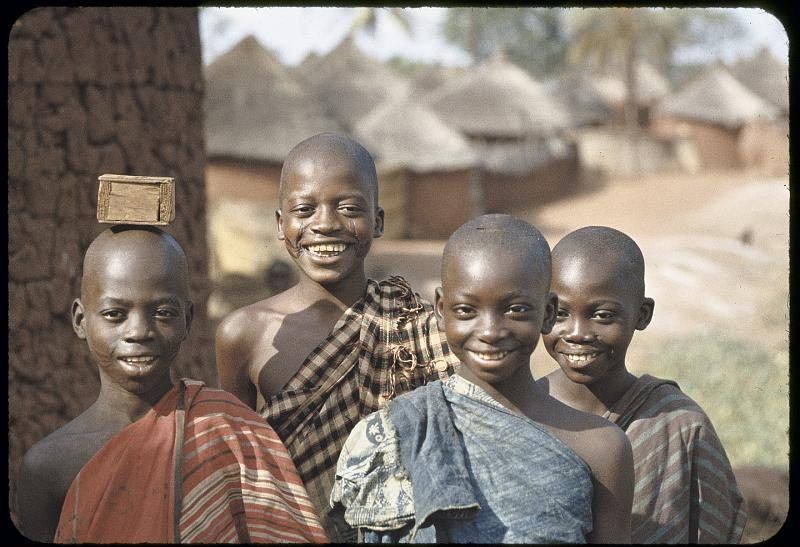 Four boys standing together in front of thatched compounds.